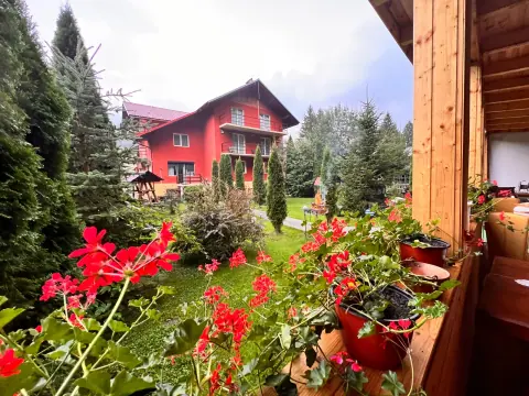 The red guesthouse facade seen through flowers and fir trees