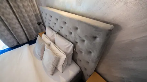 Detail of a grey headboard, cushions and white bed linen